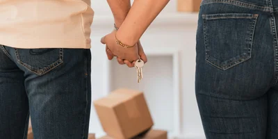 Couple holding house keys with moving boxes in the background, symbolizing Calgary townhome purchase in 2025.
