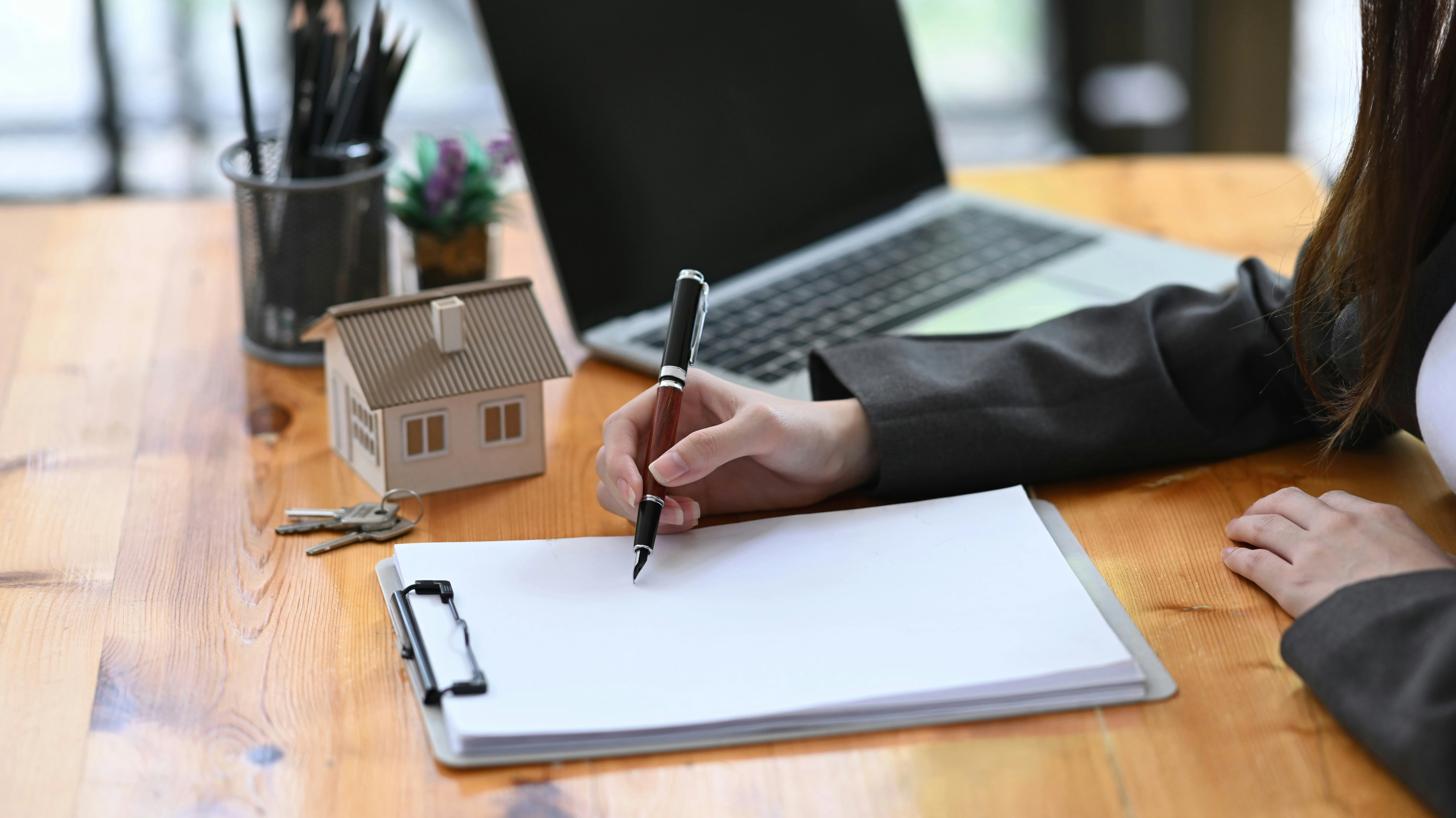 Real estate agent writing on a clipboard with house keys and model home, symbolizing hiring process in Calgary.