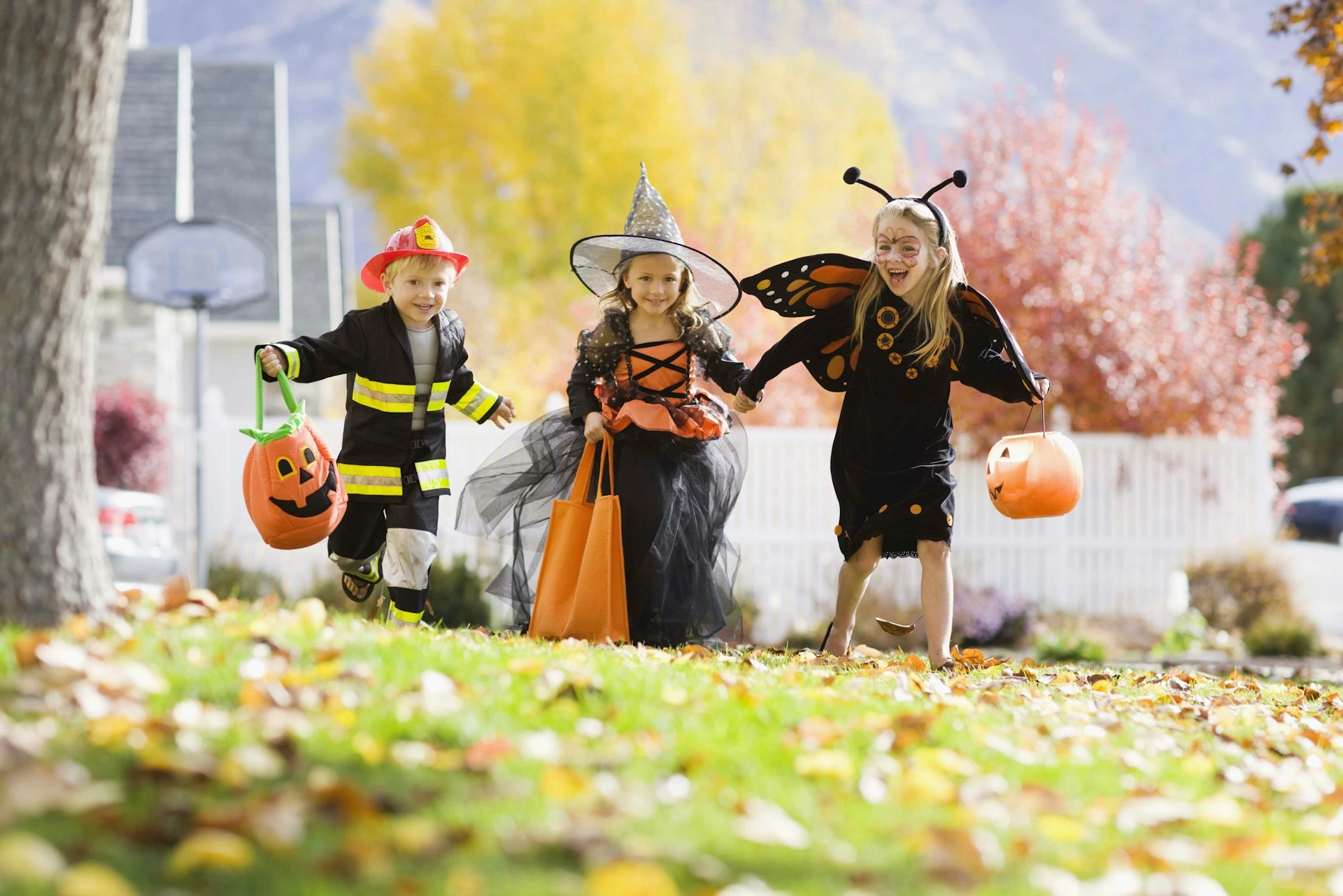Group of children dressed in Halloween costumes running through a Calgary neighbourhood with candy bags.