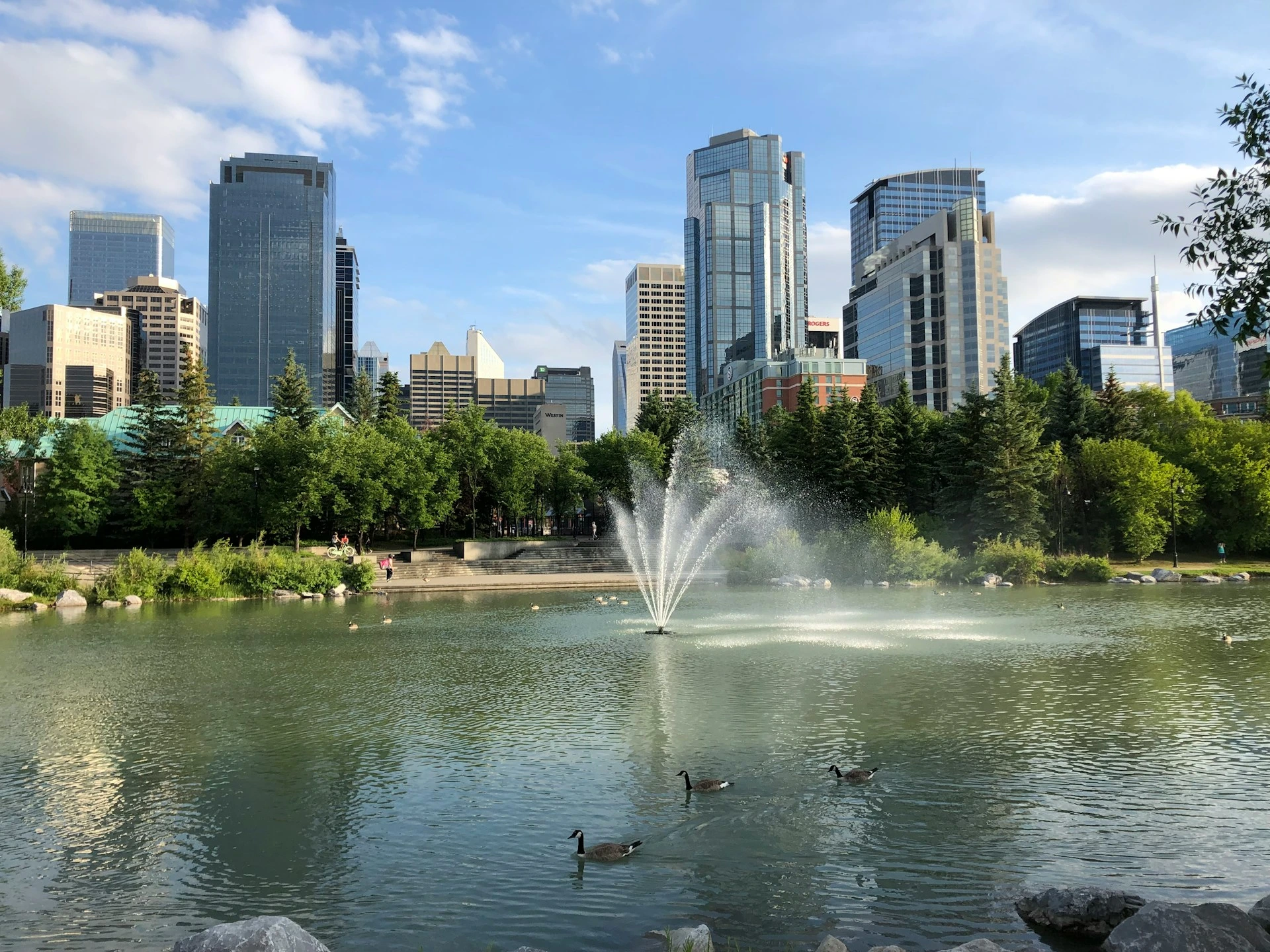 Downtown Calgary skyline view across a pond and fountain on a sunny day.