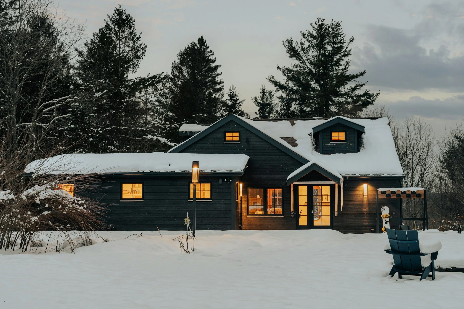 Cozy house surrounded by snow at dusk with warm interior lights glowing in winter.