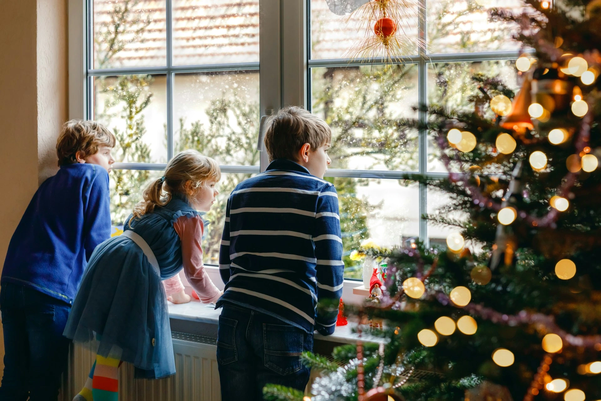 Children looking out a window at winter scenery with Christmas lights inside Calgary home.