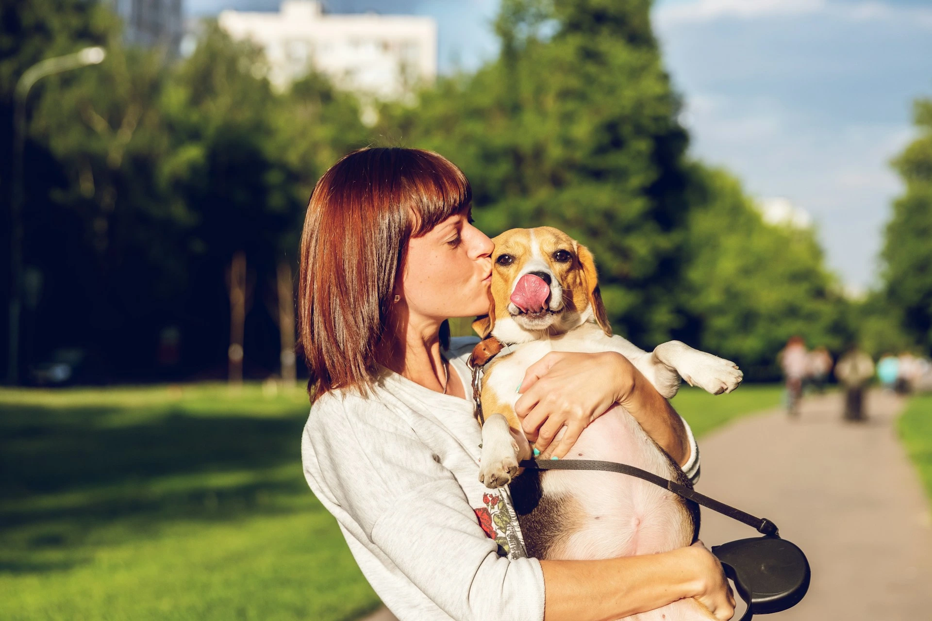 Calgary dog owner holding and kissing her beagle at a city park on a sunny day.