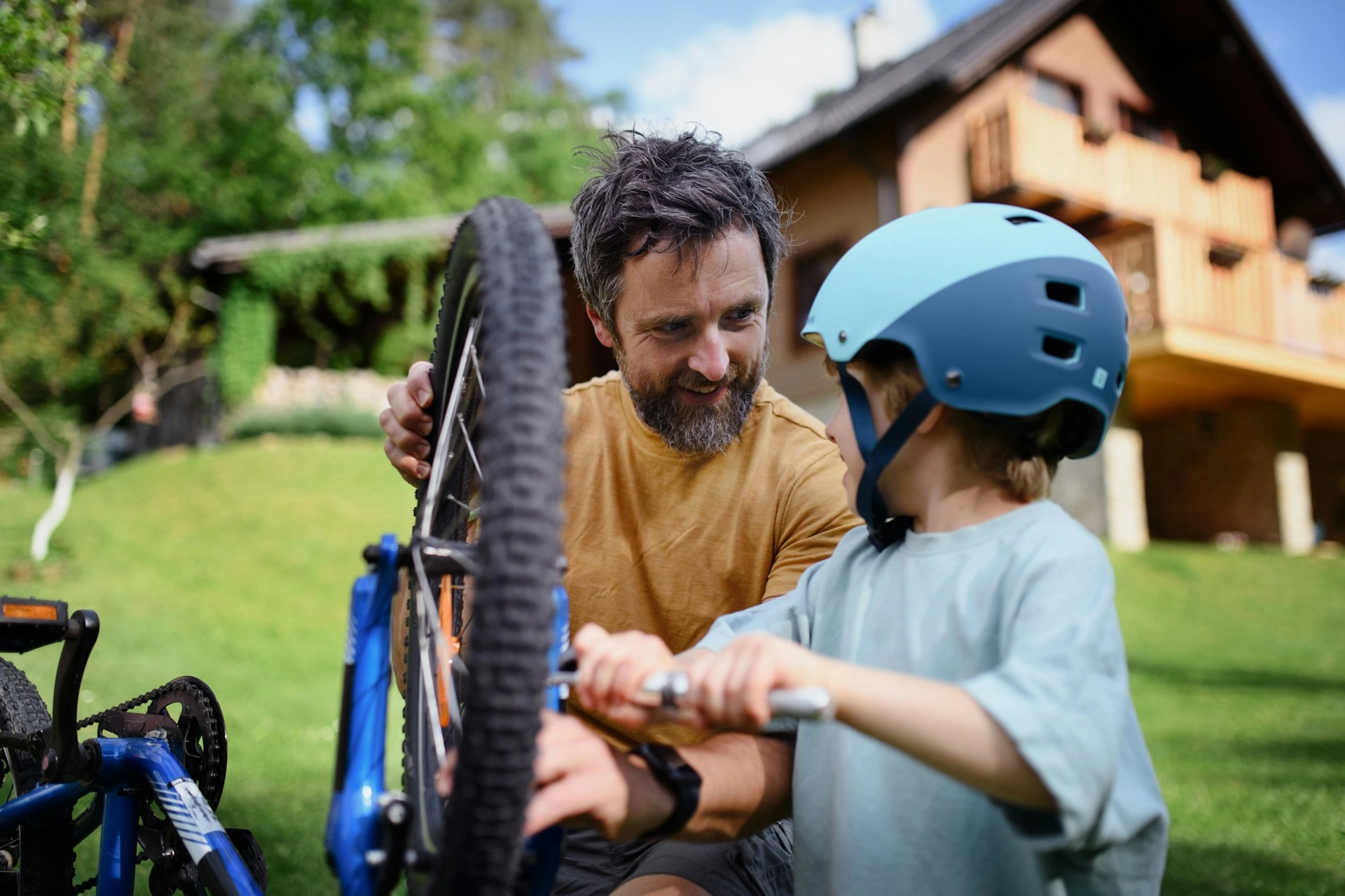 Father helping his son fix a bicycle outside their detached Calgary home in autumn.