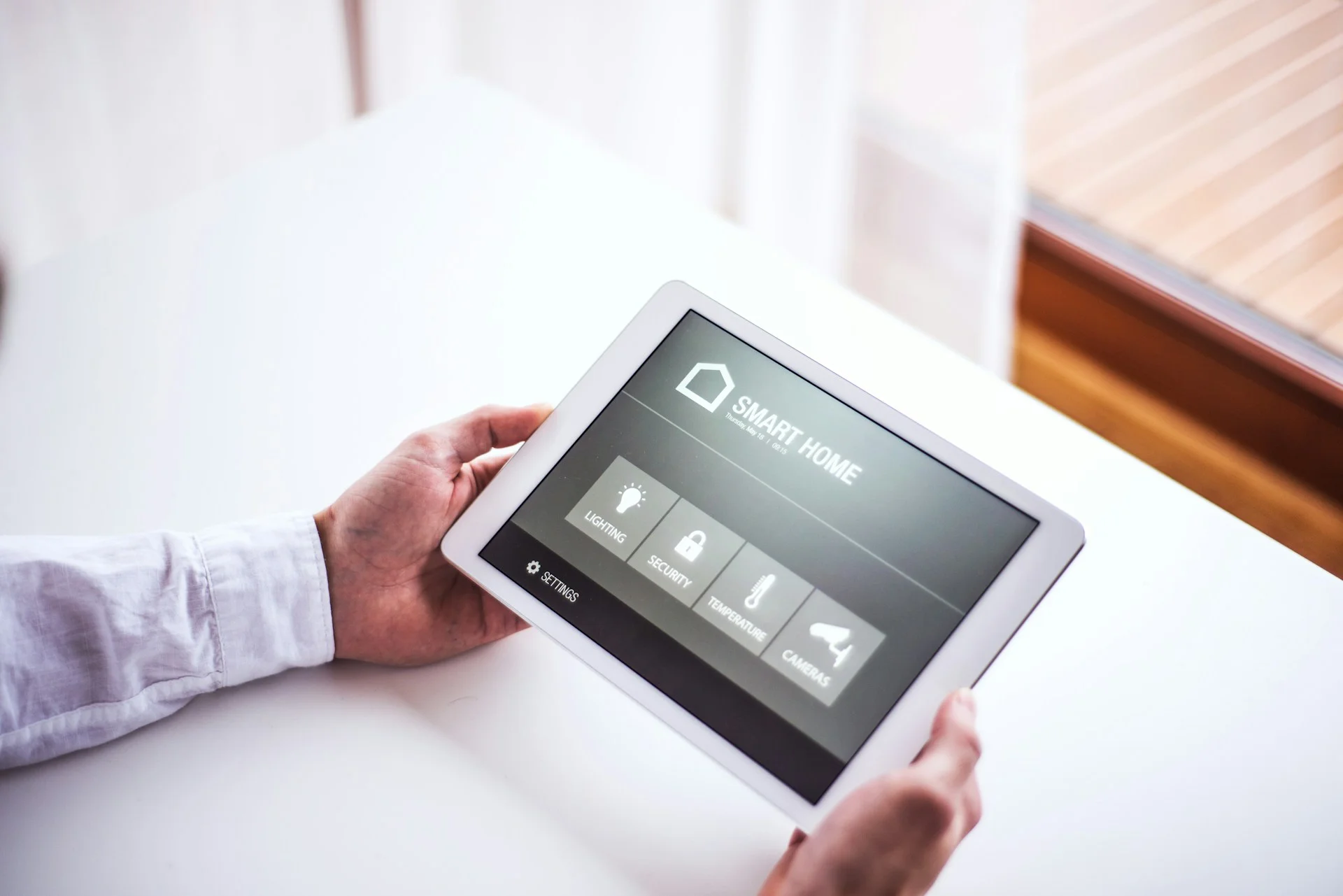 Person using a tablet to control smart home systems like lighting, temperature, and security.