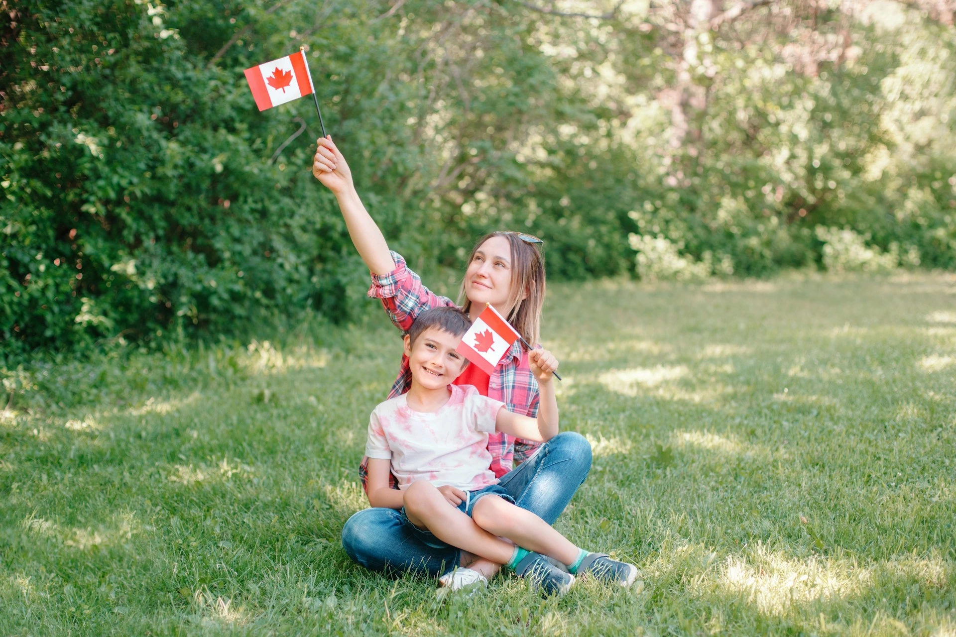 Mother and son holding Canadian flags at a Calgary park, symbolizing new homeowners.