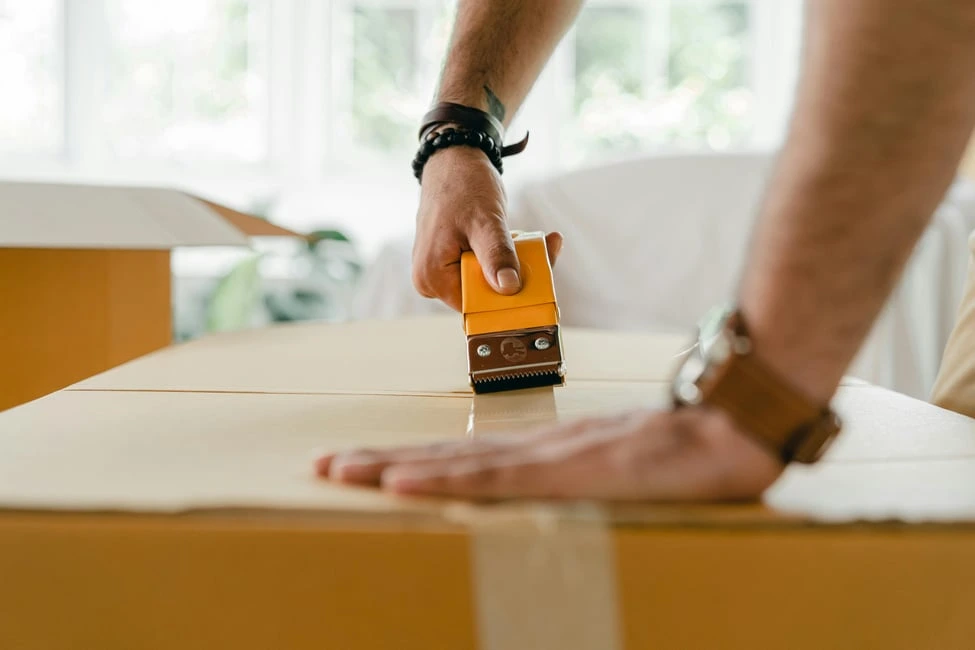 Person sealing a moving box, symbolizing Calgary homeowners preparing to buy, sell, and decide on renovations.