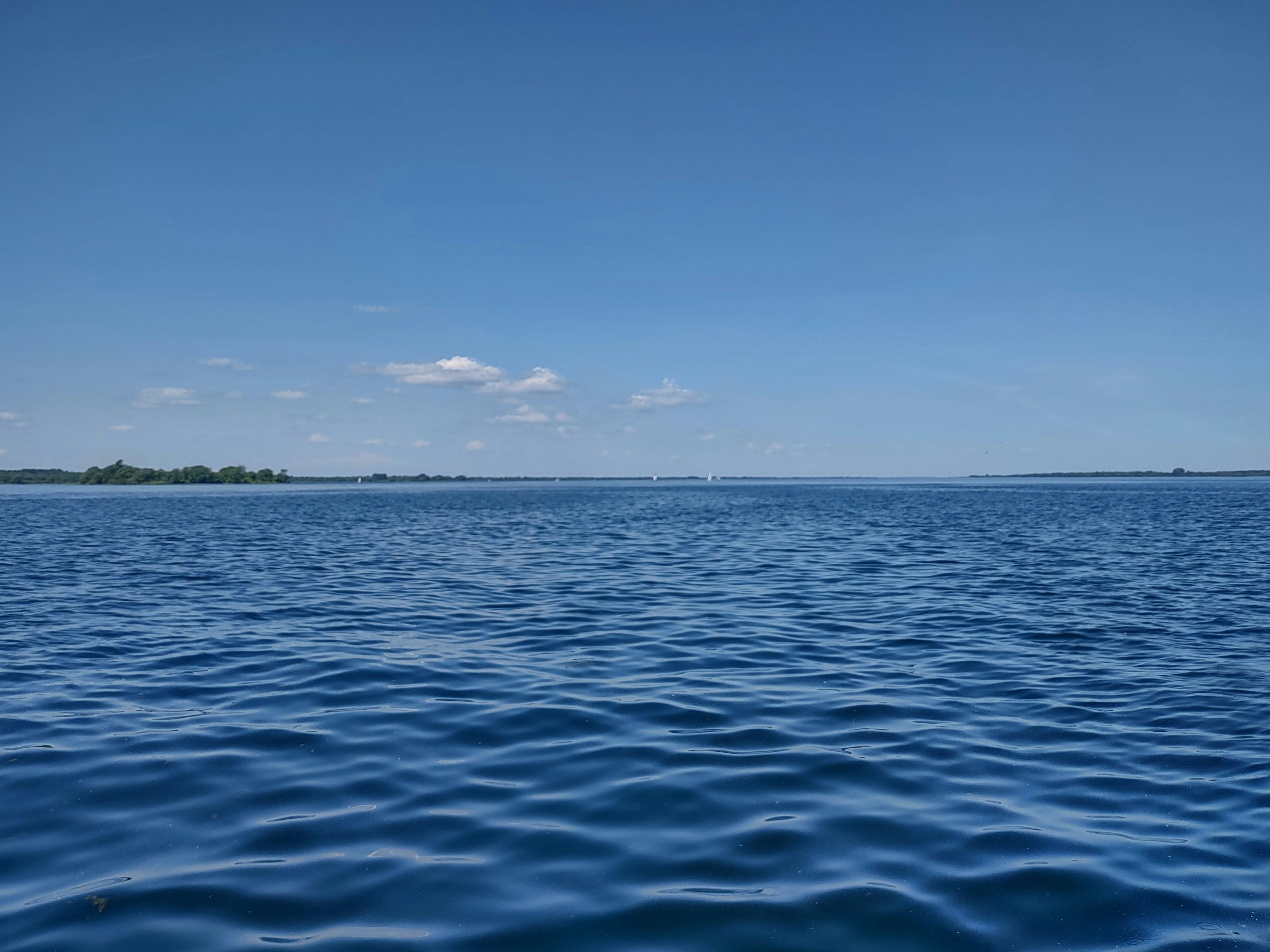 Calm blue waters of Lake Bonavista in Calgary with clear sky and distant shoreline, showcasing lakeside living appeal.