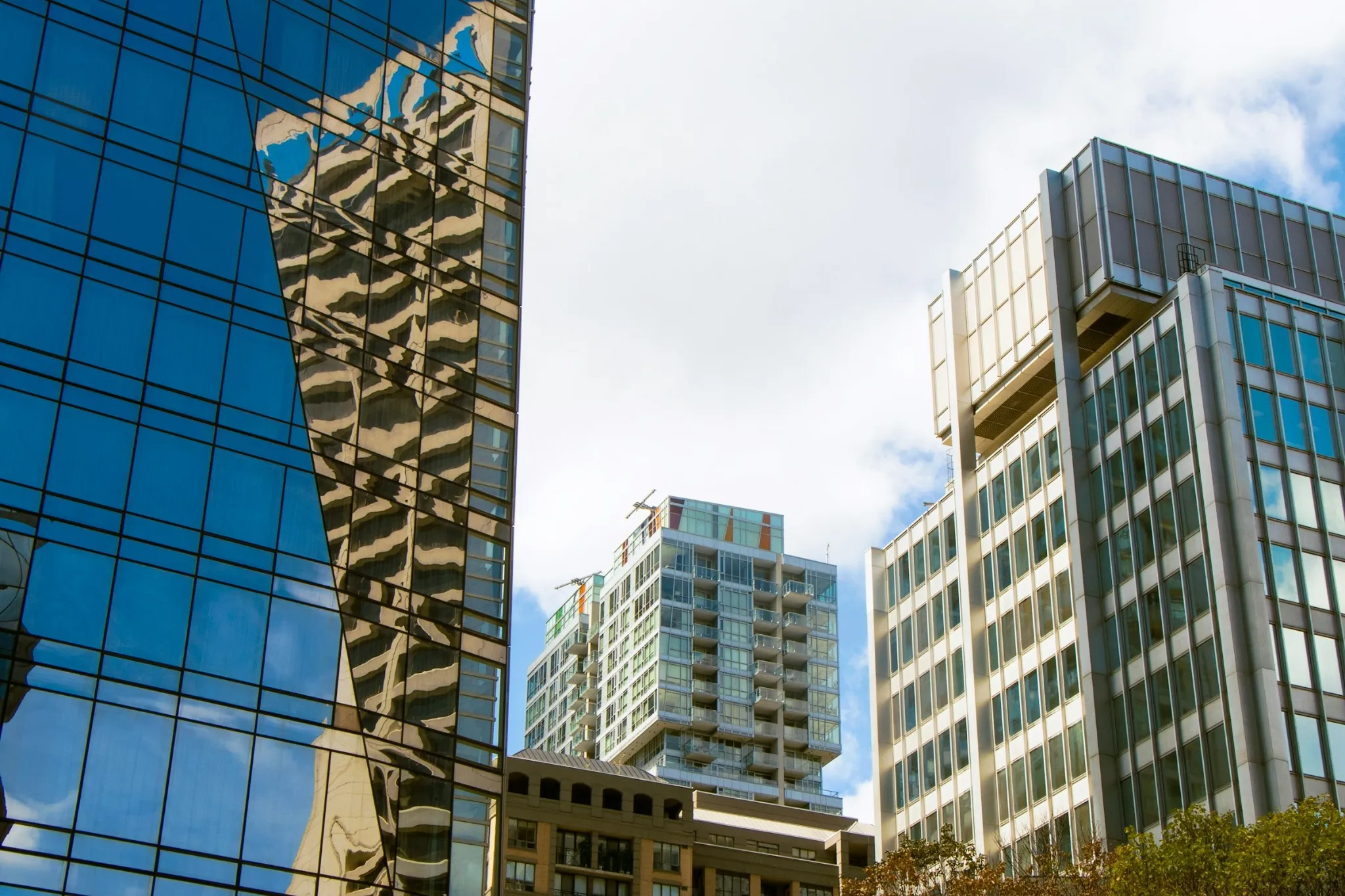 Modern Calgary condo buildings with glass exteriors reflecting city architecture under a partly cloudy sky.
