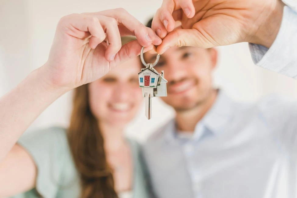 Happy couple holding house keys with a home keychain, symbolizing the true costs of owning a home in Calgary.